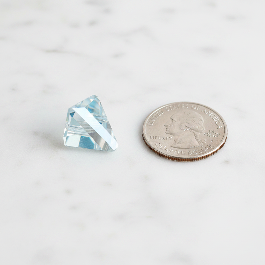 Pale blue faceted triangular prism pendant beside a U.S. quarter for size comparison.