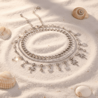 Flat lay of silver palm pendant anklet set on sand