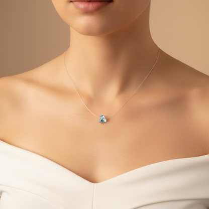 Model wearing a small pale blue triangular prism pendant on a clear illusion necklace cord.