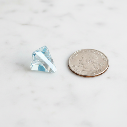 Pale blue faceted triangular prism pendant beside a U.S. quarter for size comparison.